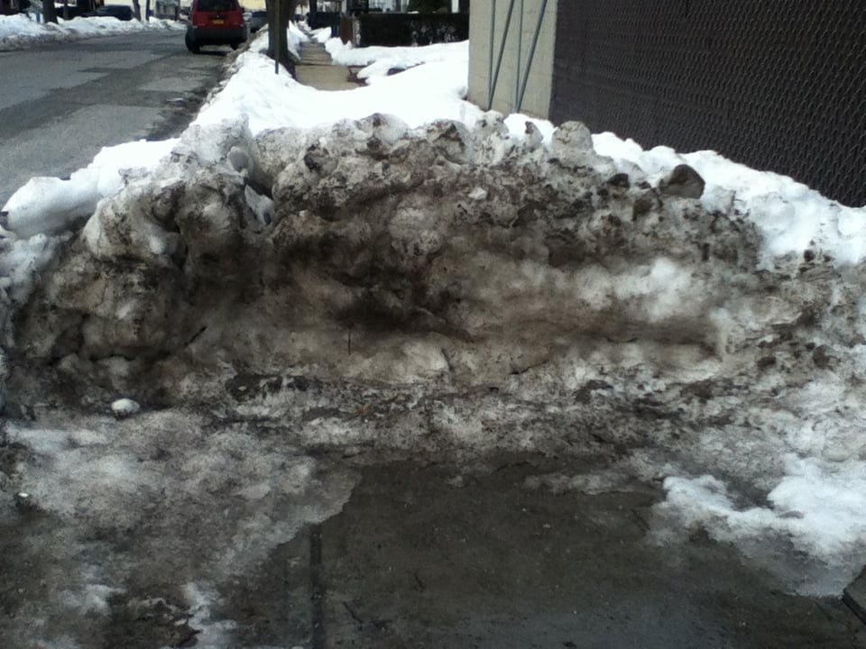 A huge, dirty pile of snow blocking the middle of the sidewalk.